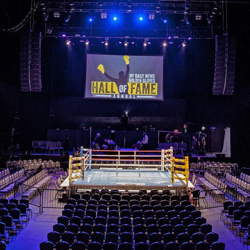 A boxing ring set in a spacious arena, featuring a large screen above for displaying event details.